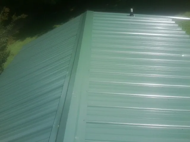 New green metal panels meeting at the ridge of a roof — Flat Roof Repair work by our crew in Pottsville