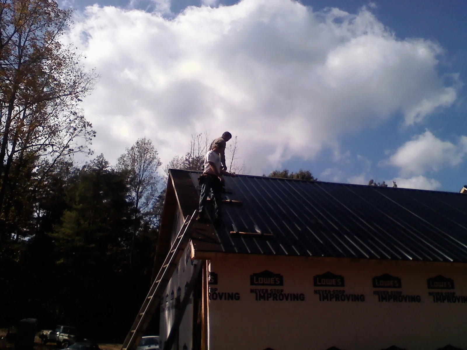 Roofer fastening dark metal panels high against a cloudy sky, from a Roof Inspection job in Pottsville