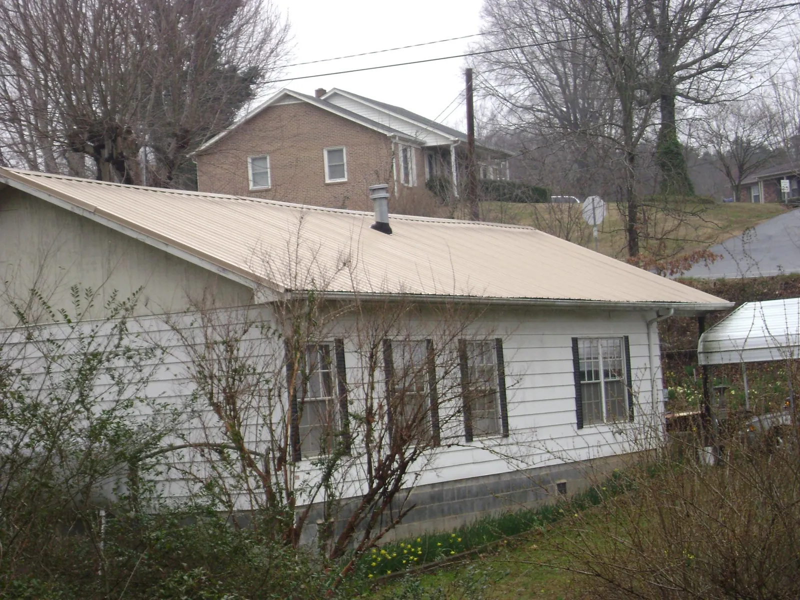 Tan metal roof on a white sided house set into a hillside — Commercial Roofing by Roofing Brothers in Pottsville